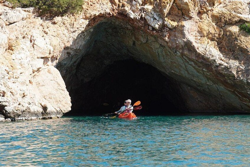 A person kayaking in a body of water with a rocky cave entrance in the background. 3