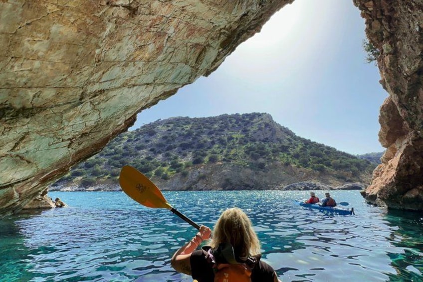 A kayaker in a cave opening, a rocky coastline, and a distant hill. 1