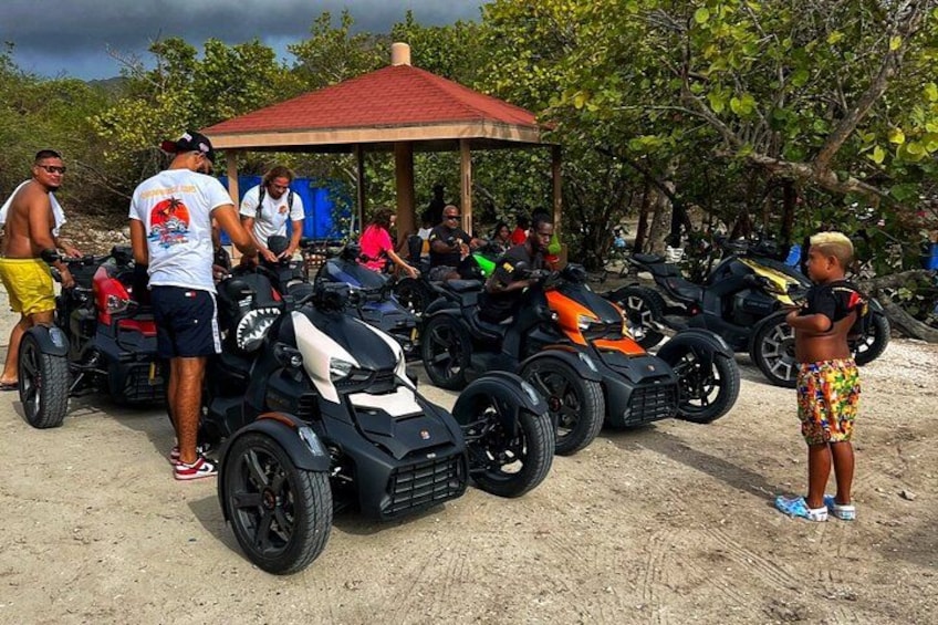 Eine Gruppe von Menschen um Quads an einem sandigen Strand, im Hintergrund ein Pavillon. 5