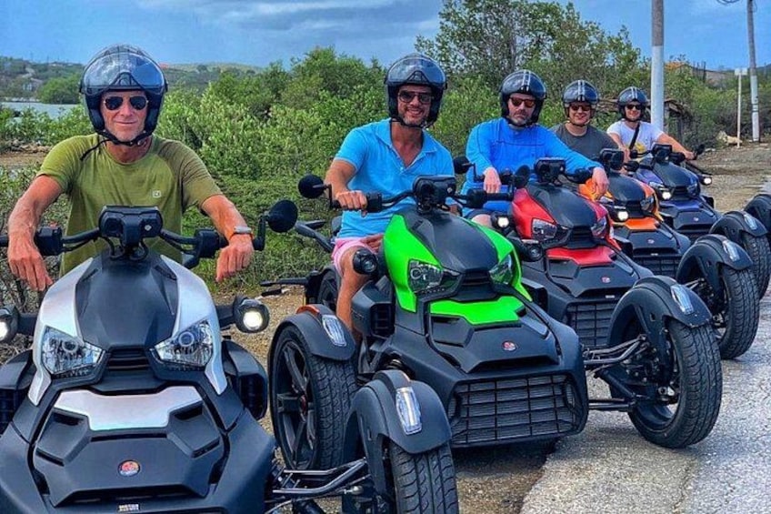 Four people riding quad bikes on a paved path with greenery in the background. 2