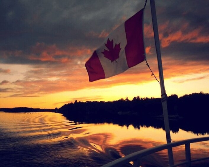 A Canadian flag on a pole, a body of water, and a sunset sky. 3