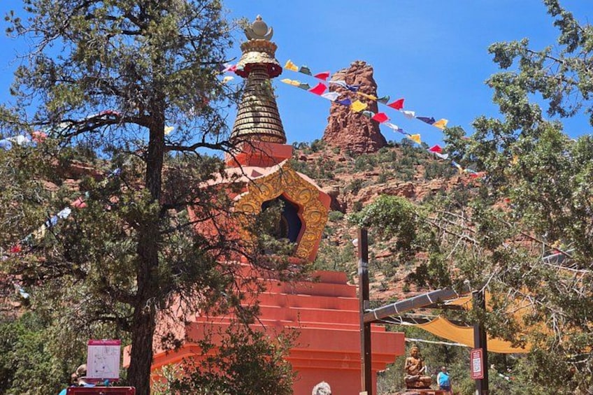 A red building with a golden spire, surrounded by trees and a rocky hill. 3