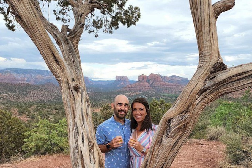 A man and a woman standing in front of a tree with a scenic view of red rock formations in the background. 1