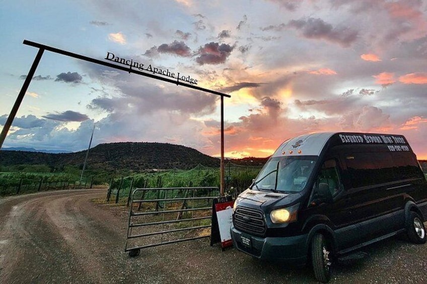 A black van parked by a gate labeled 'Dancing Apache Lodge' with a sunset in the background. 2