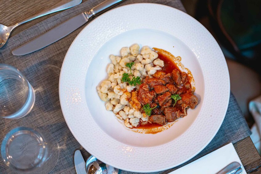 A plate of food with a meat dish and pasta, accompanied by a glass of water and cutlery on a table. 3