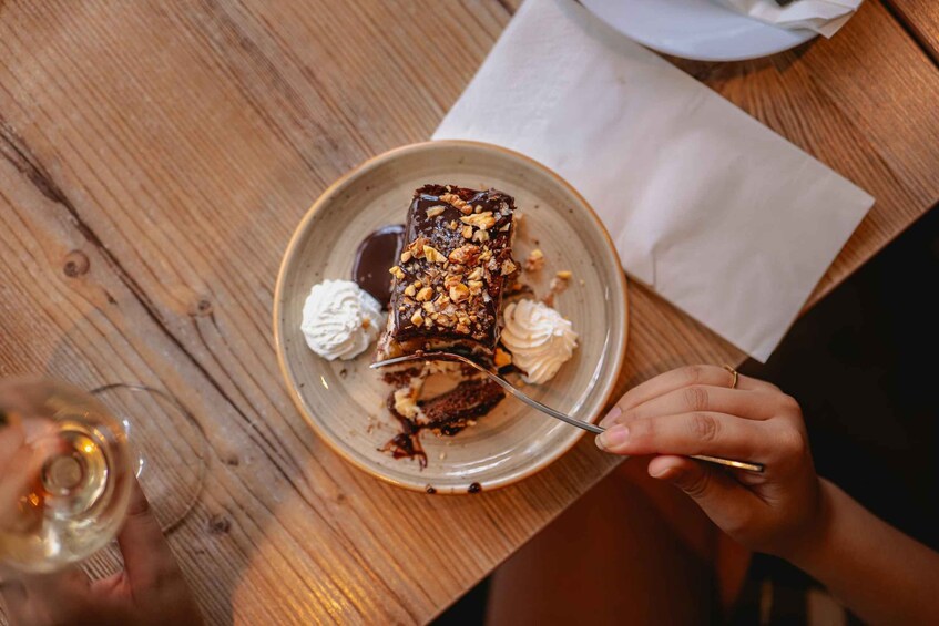 A person holding a fork with a slice of cake on a plate, with whipped cream on the side. 4