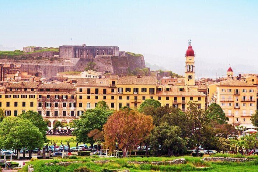 A cityscape with historic buildings, a prominent clock tower, and a large fortress in the background. 4
