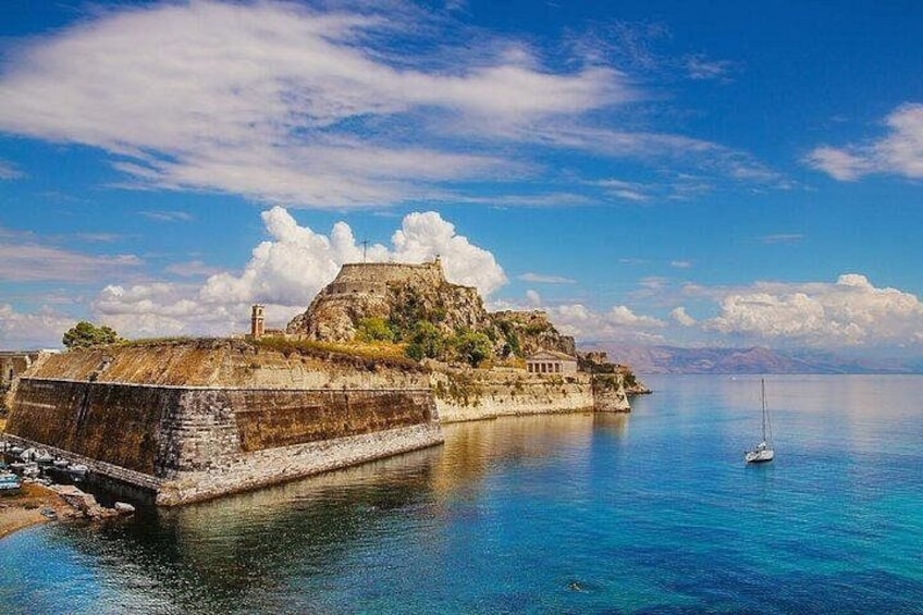 A coastal fortification with a clear view of the sea, a sailboat, and a distant mountain range. 3
