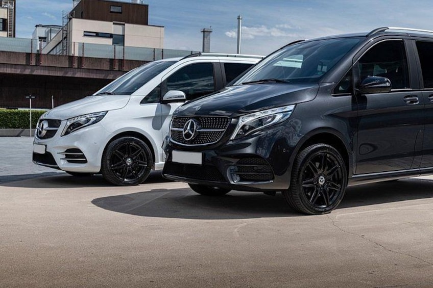 Dos vehículos Mercedes-Benz estacionados en un estacionamiento con edificios al fondo. 2