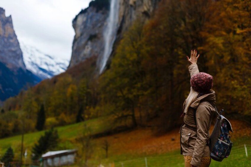 A person standing with arms raised, facing a mountainous landscape with a waterfall. 3