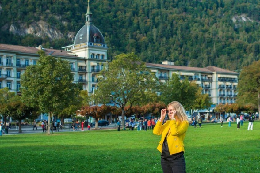 A person in a yellow jacket standing in a grassy field with a building and trees in the background. 4