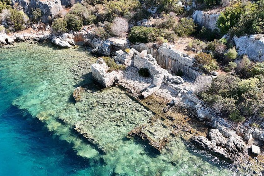 A coastal landscape with clear turquoise waters, rocky terrain, and ancient ruins. 5