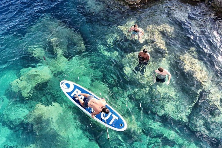 Eine Person steht auf einem Paddleboard in klarem, blauem Wasser vor steinigen Felsformationen. 2