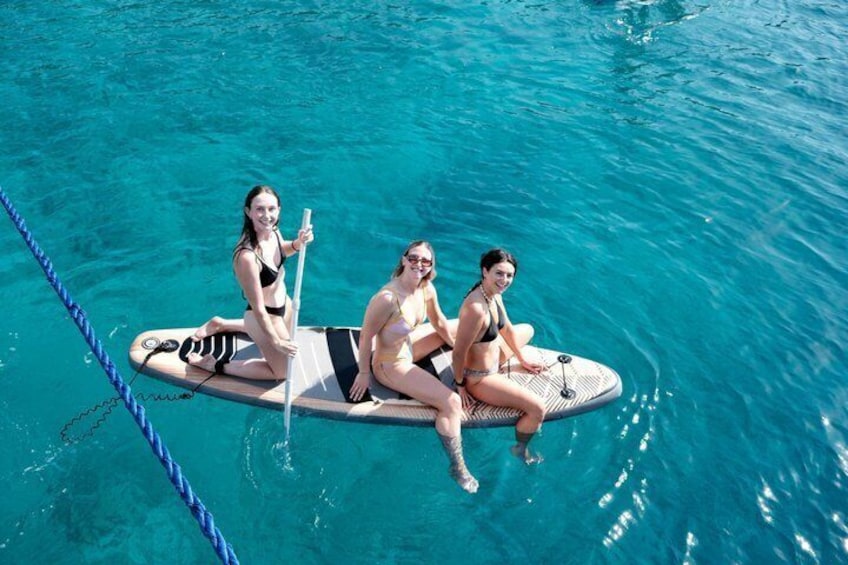 Three people on a paddleboard in a clear blue pool. 4