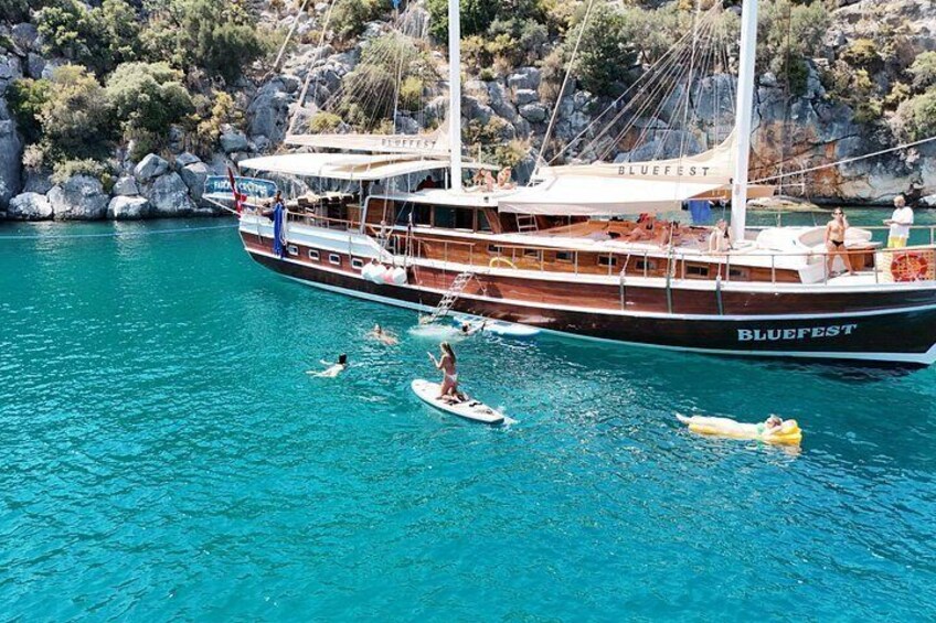 Un bote llamado 'BLUEFEST' con gente nadando y flotando en el agua. 2
