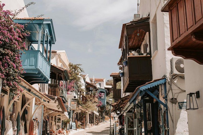A narrow street lined with colorful buildings, some with balconies and shutters, under a clear sky. 3