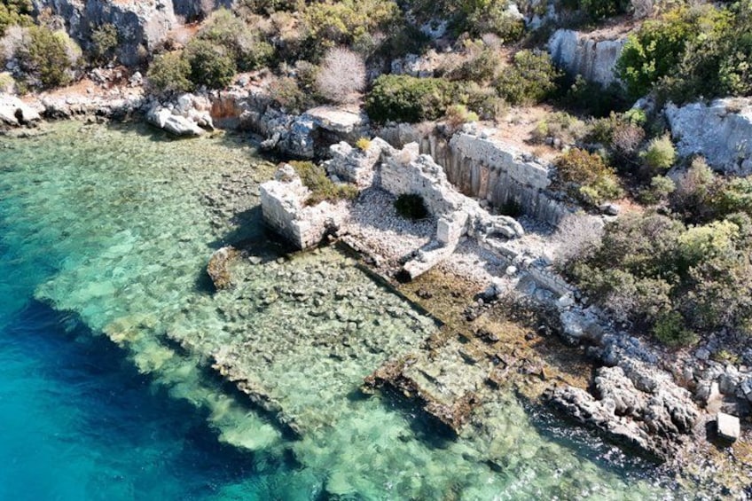 Un paysage côtier caractérisé par des eaux turquoise limpides, un terrain rocheux et des ruines antiques. 2