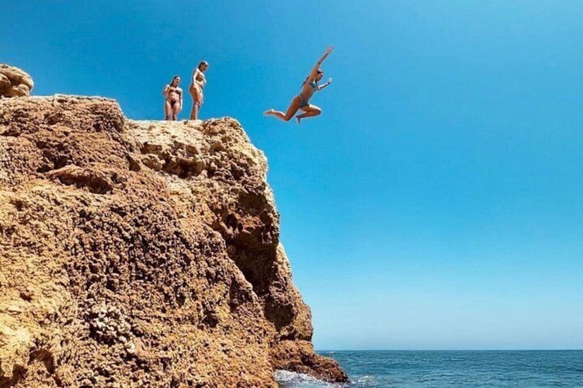 A rocky cliff with two people standing at the edge and one person diving into the water. 4