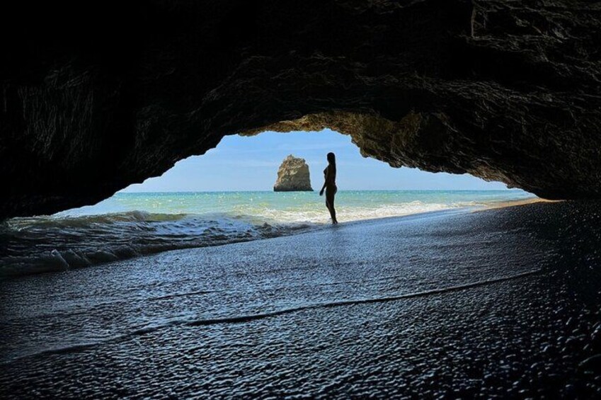 A person standing on a beach with waves crashing in the background, viewed through a cave entrance. 4