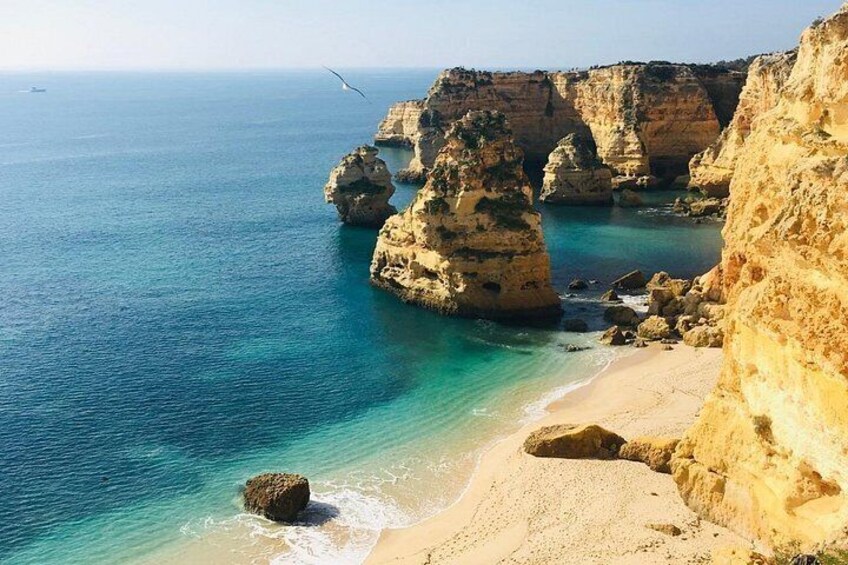A coastal landscape with cliffs, clear blue water, and a sandy beach. 3