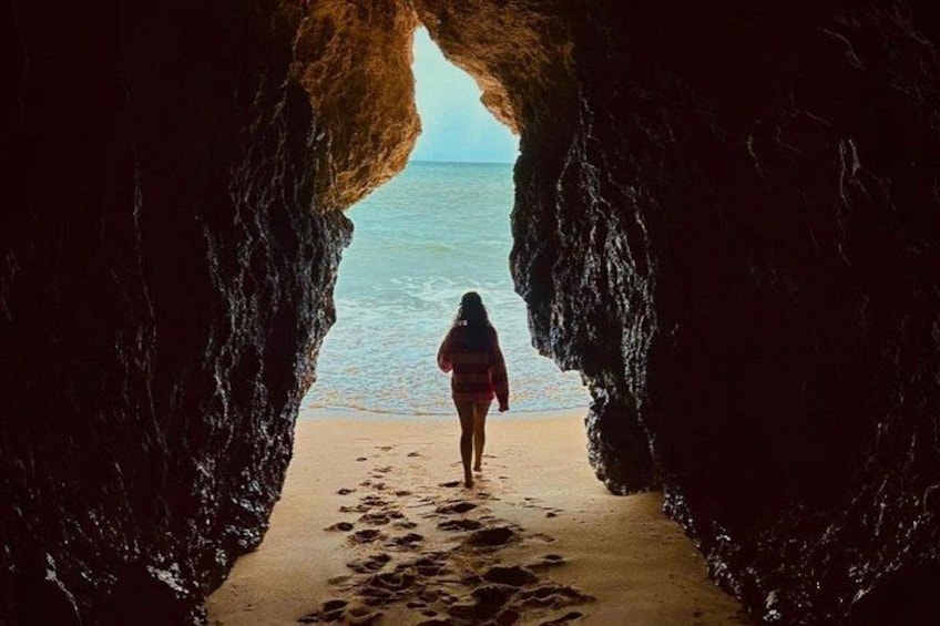 Una persona caminando por la playa a través de un arco natural de roca. 2
