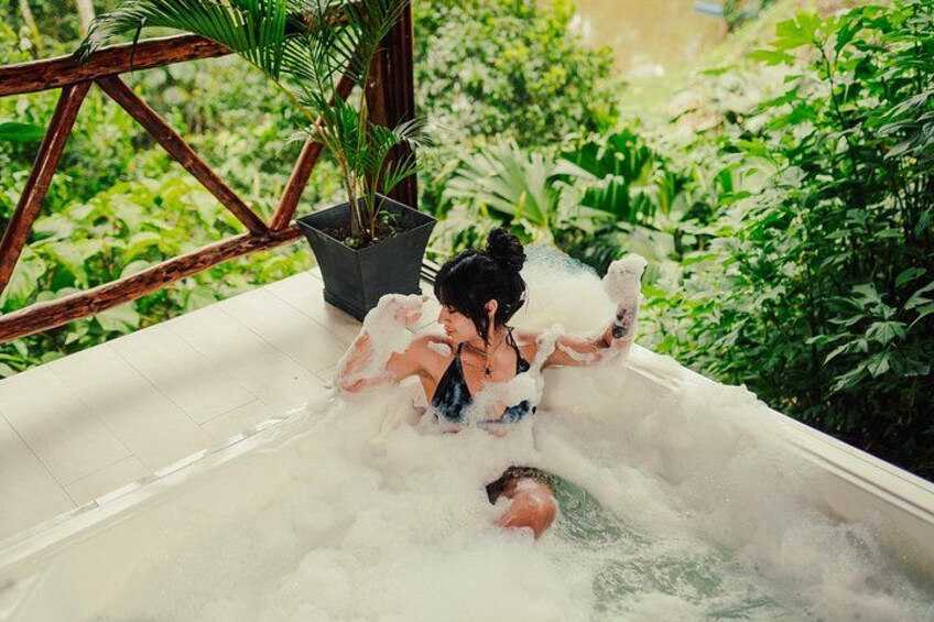 A person in a bathtub filled with bubbles, surrounded by greenery. 2