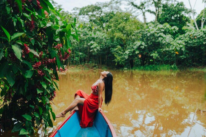 A person in a red dress sitting on a blue boat in a flooded area with dense greenery in the background. 3