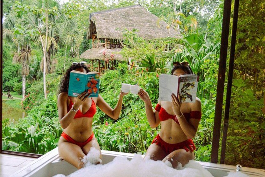 Two people in a hot tub surrounded by lush greenery and a thatched-roof structure. 4