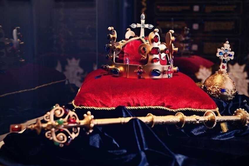 A richly decorated royal throne with a red cushion, ornate gold and red jewels, and a cross atop. 1