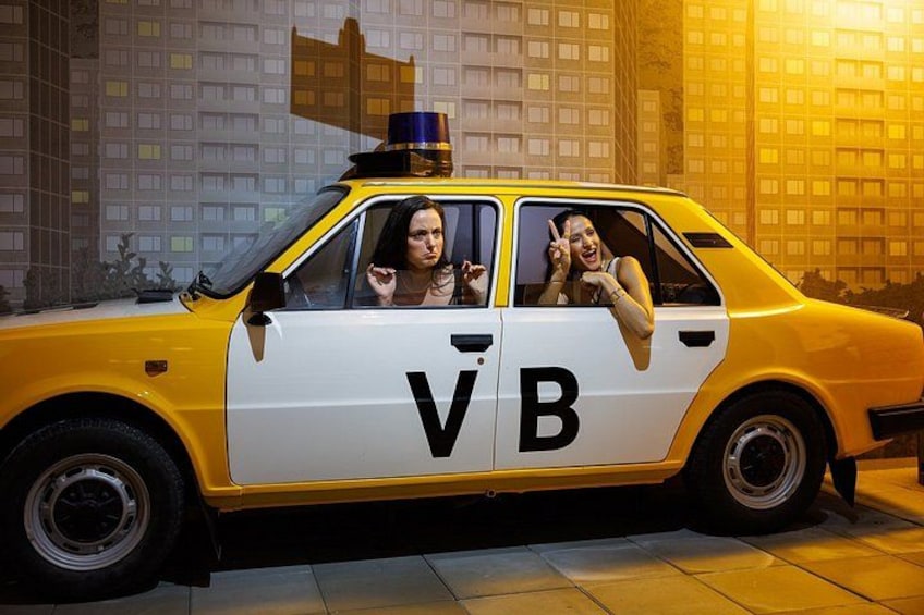 Een gele en witte taxi met 'V B' op de zijkant, geparkeerd in een stedelijke omgeving. 1