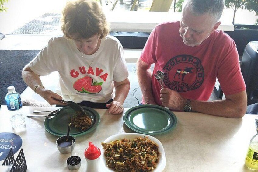 Two people sitting at a table with plates of food, a bottle of water, and condiments. 3