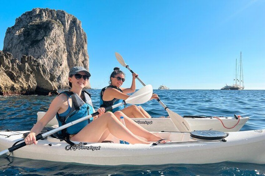 Två personer paddlar kajak på ett lugnt hav med en klippig udde i bakgrunden. 2