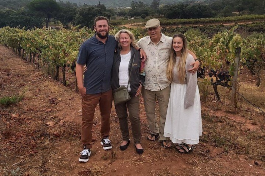 Un gruppo di persone in piedi in un vigneto con file di viti. 1