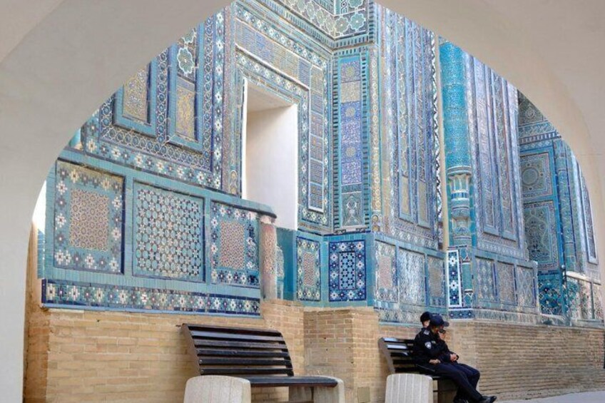 Una persona sentada en un banco frente a un edificio con elaborados diseños de azulejos azules y blancos. 5