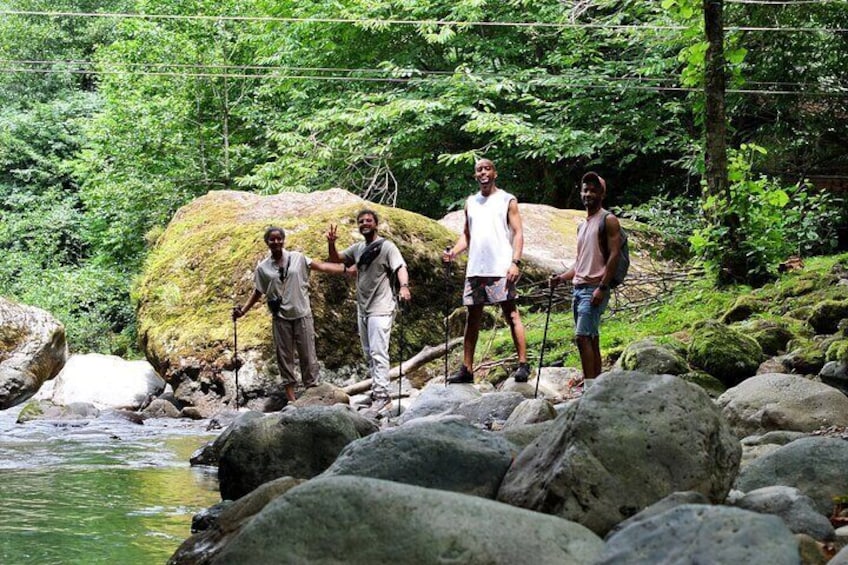 Three people standing on rocks by a river in a forested area. 1