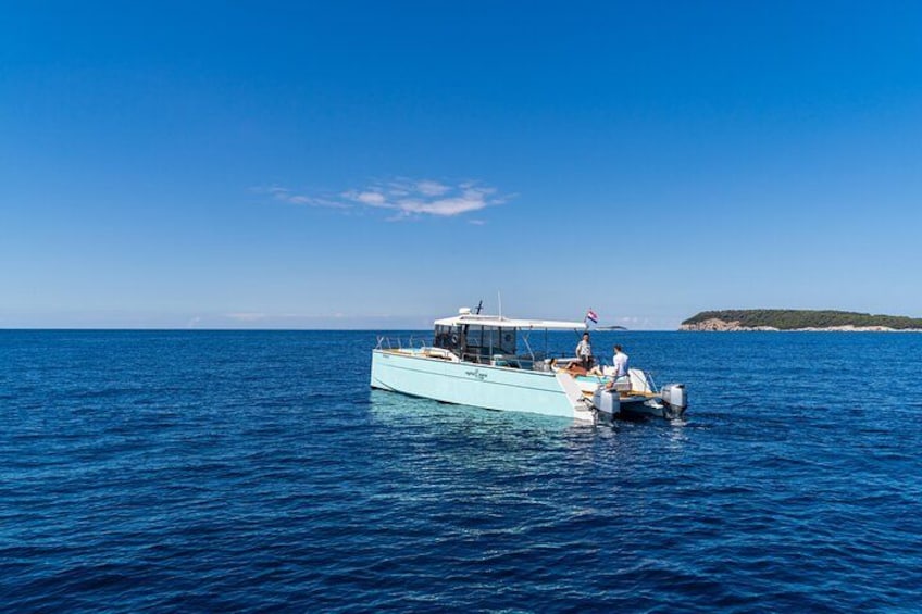 Un barco azul claro con dos personas en la cubierta, navegando sobre un mar tranquilo. 3