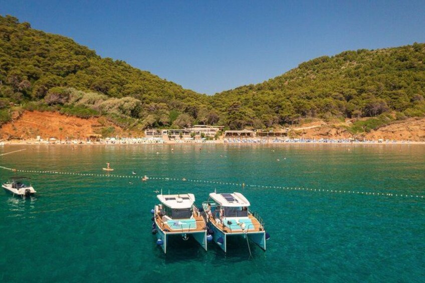 A coastal area with boats docked, clear turquoise water, and a hilly landscape in the background. 2