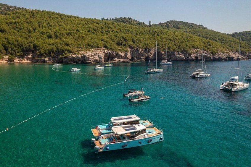 A turquoise sea with boats anchored near a forested coastline. 4