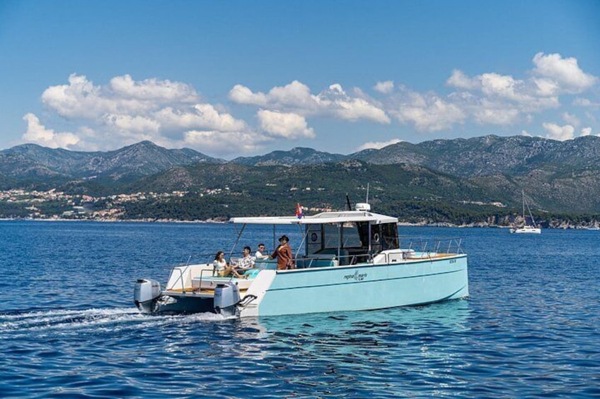 Un petit bateau bleu clair avec des passagers à bord, naviguant sur une mer calme, avec des montagnes en arrière-plan et un ciel dégagé. 3