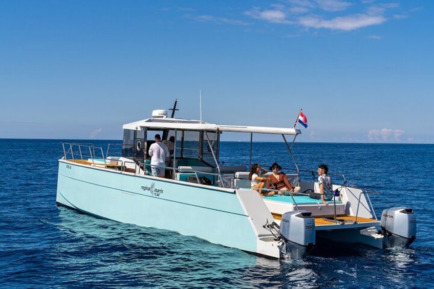 Una embarcación azul claro con una bandera, personas a bordo y agua azul tranquila. 2