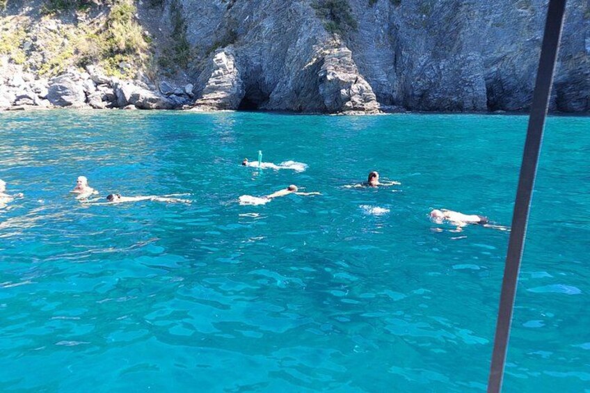 People swimming in clear blue water with rocky cliffs in the background. 3