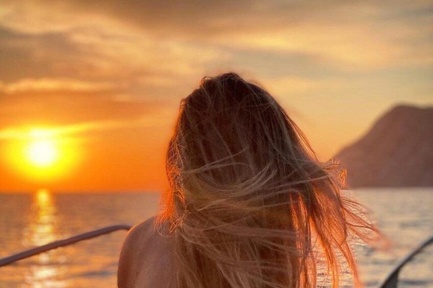 A person with blonde hair looking at a sunset over the ocean. 4