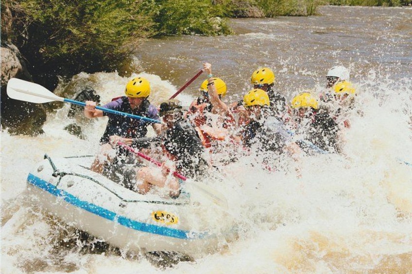 A group of people in a white raft with blue trim paddling through a river with white water. 2