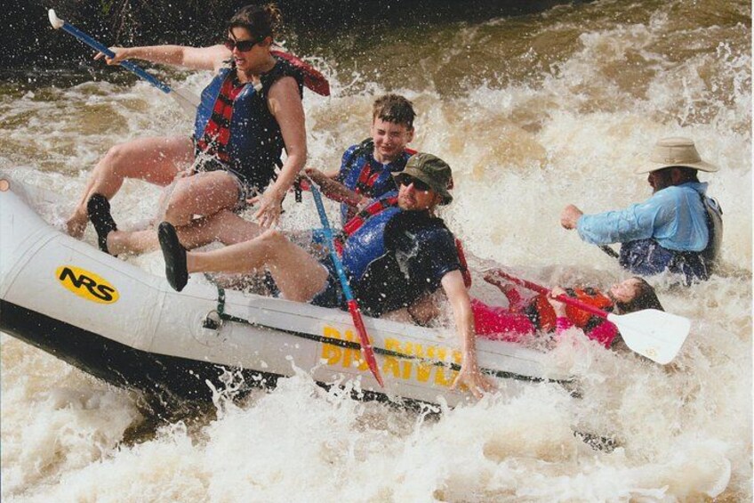 Des personnes se trouvent dans un radeau blanc aux couleurs bleue et rouge, et le font avancer en pagayant sur une rivière. 2