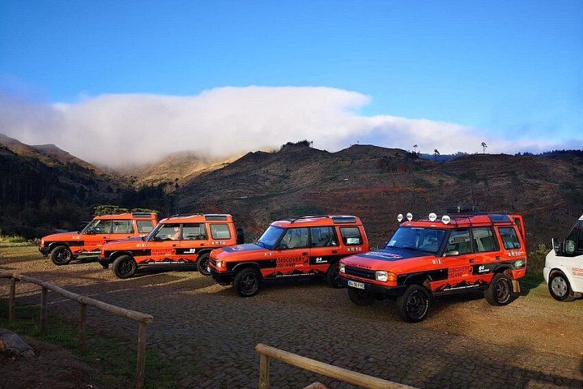 Cuatro vehículos todoterreno rojos estacionados en un camino adoquinado, con un paisaje montañoso al fondo. 2