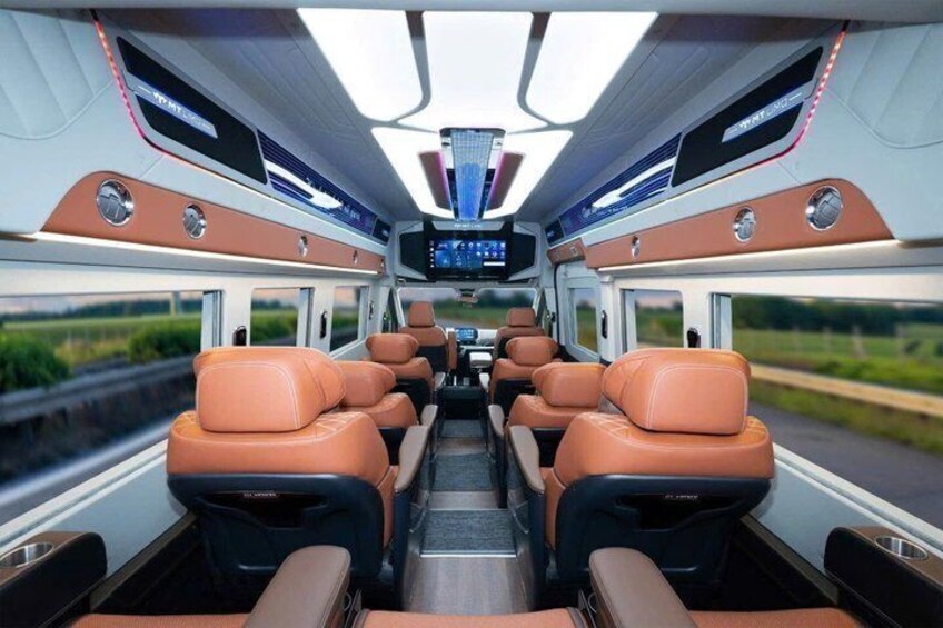 Interior de un tren con asientos de cuero, compartimentos superiores para equipaje y una pantalla digital. 3