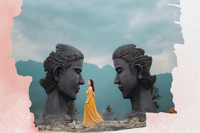 A sculpture of two faces with a person in a yellow dress standing between them. 2