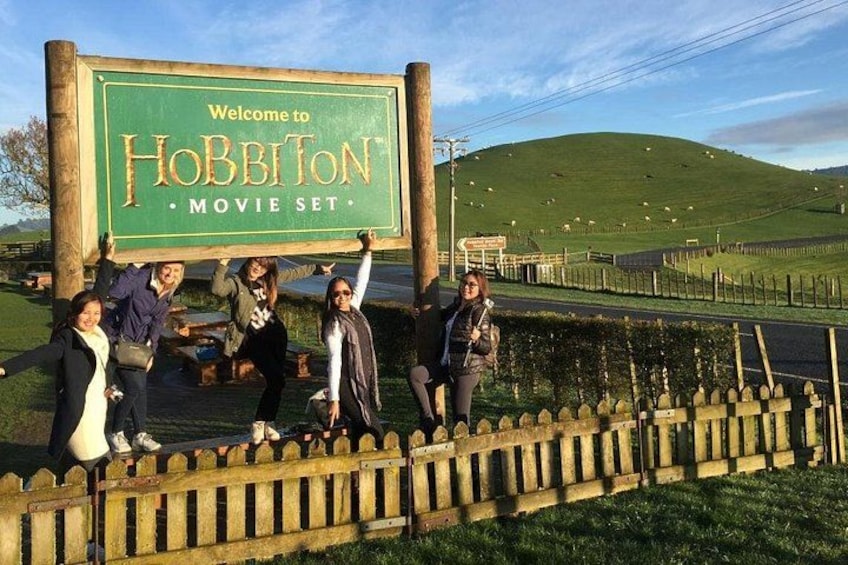 A group of people holding a sign that says 'Welcome to Hobbiton Movie Set.' 3
