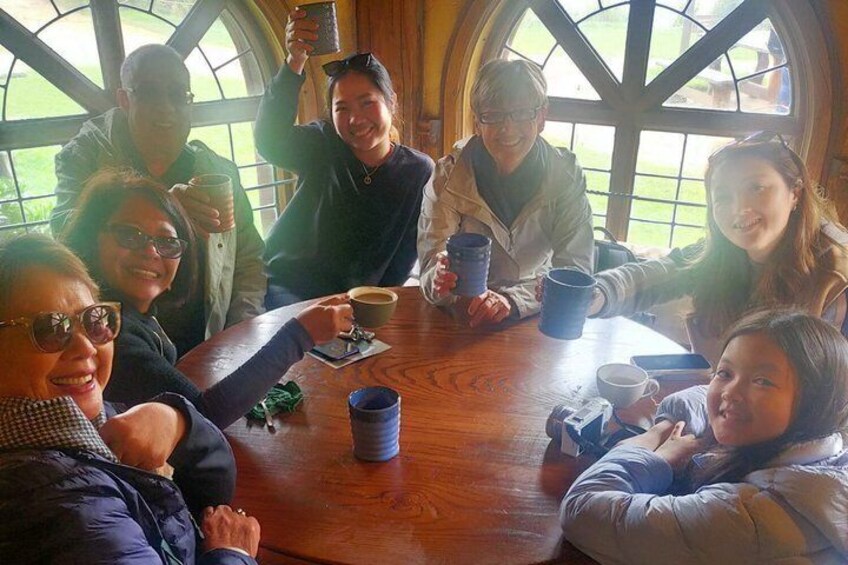 A group of people sitting around a wooden table with coffee cups, in a room with large windows. 4