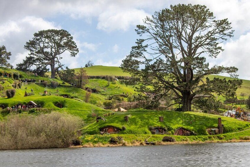 A lush green landscape with rolling hills, a large tree, and a small house by a body of water. 5